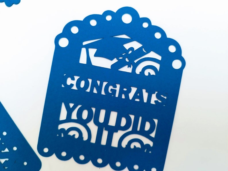 May include: Blue paper cutout with a graduation cap and diploma design. The text "Congrats You Did It" is cut out of the paper.