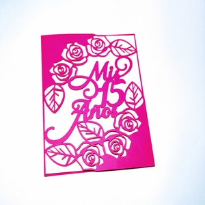 May include: A pink card with a cut-out design of roses and leaves. The text "Mis 15 Anos" is written in a decorative font.