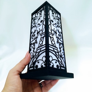 May include: Black and white paper cut-out lamp with a design of the Eiffel Tower and floral accents. The lamp is on a black base.