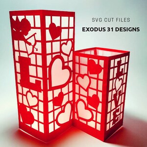 May include: Two red paper lanterns with cut-out designs of hearts and the word "LOVE". The lanterns are lit from inside, creating a warm glow. SVG cut files by Exodus 31 Designs.