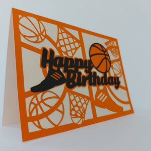 May include: Orange card with a white interior and a black cut-out design of basketballs, sneakers, and a basketball hoop. The text "Happy Birthday" is cut out in black.