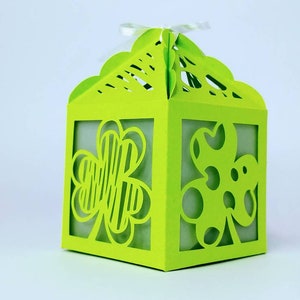 May include: A green paper gift box with a shamrock design. The box has a cut-out design that allows you to see through the sides.