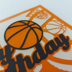 May include: Orange and black paper cut-out card with a basketball and the words "Happy Birthday".