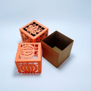 May include: Three decorative boxes, one with a pumpkin design, one with a leaf design, and one plain brown box. The boxes are made of orange paper and are all the same size.