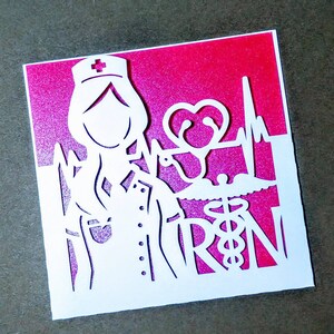 May include: White paper cut-out card with a pink background. The card features a nurse with a stethoscope, a heart, and the letters "RN" with a medical symbol.