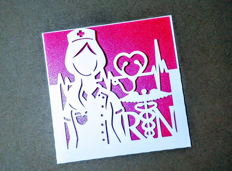 May include: White paper cut-out card with a pink background. The card features a nurse with a stethoscope, a heart, and the letters "RN" with a medical symbol.