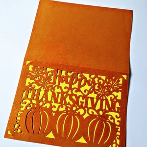 Puede incluir: Tarjeta naranja con un inserto amarillo. La tarjeta tiene un dise&ntilde;o recortado de calabazas, hojas y las palabras "Feliz D&iacute;a de Acci&oacute;n de Gracias".