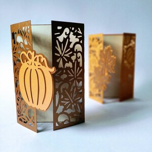 May include: Two brown cardstock paper crafts with intricate cut-out designs. One features a pumpkin with a stem and leaves. Both have a white background.