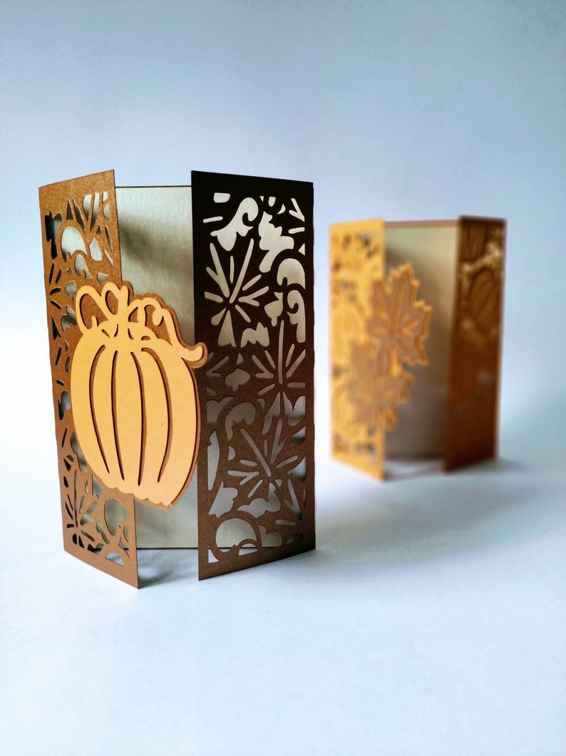 May include: Two brown cardstock paper crafts with intricate cut-out designs. One features a pumpkin with a stem and leaves. Both have a white background.