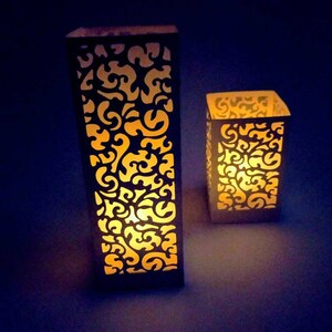 May include: Two white paper lanterns with intricate cut-out designs, illuminated from within, casting a warm glow.