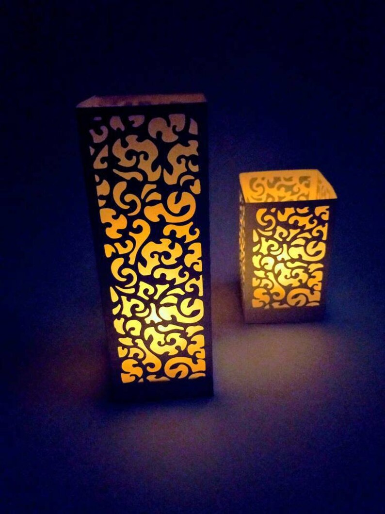 May include: Two white paper lanterns with intricate cut-out designs, illuminated from within, casting a warm glow.