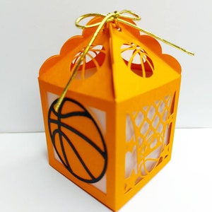 May include: Orange paper gift box with a basketball design and a gold ribbon. The box has a cut-out design of a basketball net and a basketball.