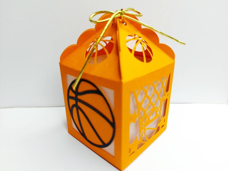 May include: Orange paper gift box with a basketball design and a gold ribbon. The box has a cut-out design of a basketball net and a basketball.