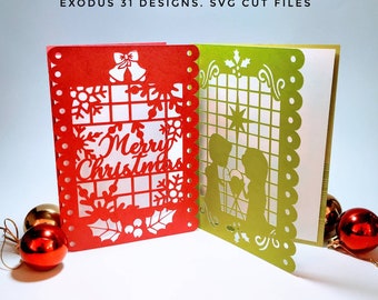 May include: Two Christmas cards with intricate cut-out designs. The red card features a snowflake and holly design with the text "Merry Christmas". The green card features a nativity scene with a star and holly.
