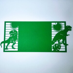 May include: Green cardstock cut-out with two dinosaurs, one on each side. The dinosaurs are facing each other and are surrounded by palm trees and leaves. The cardstock is blank in the middle.
