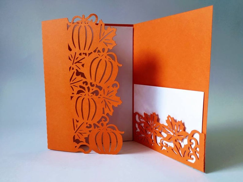 May include: Orange card with a cut-out design of pumpkins and leaves. The card is folded in half and has a white insert.