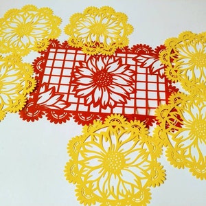 Puede incluir: Un conjunto de siete servilletas de papel con un dise&ntilde;o de girasol. Las servilletas son amarillas y rojas, y est&aacute;n dispuestas en c&iacute;rculo alrededor de un cuadrado rojo con un patr&oacute;n de cuadr&iacute;cula blanca.