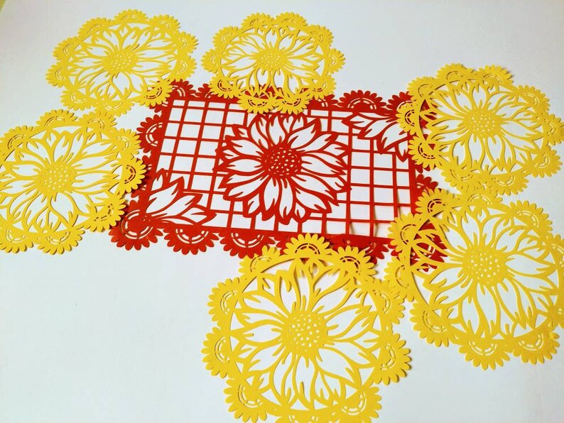 Puede incluir: Un conjunto de siete servilletas de papel con un dise&ntilde;o de girasol. Las servilletas son amarillas y rojas, y est&aacute;n dispuestas en c&iacute;rculo alrededor de un cuadrado rojo con un patr&oacute;n de cuadr&iacute;cula blanca.