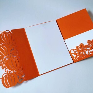 May include: Orange card with a white insert and a cut-out design of pumpkins and leaves. The card is folded in half and the insert is visible.
