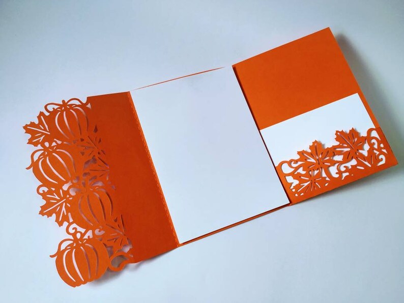 May include: Orange card with a white insert and a cut-out design of pumpkins and leaves. The card is folded in half and the insert is visible.