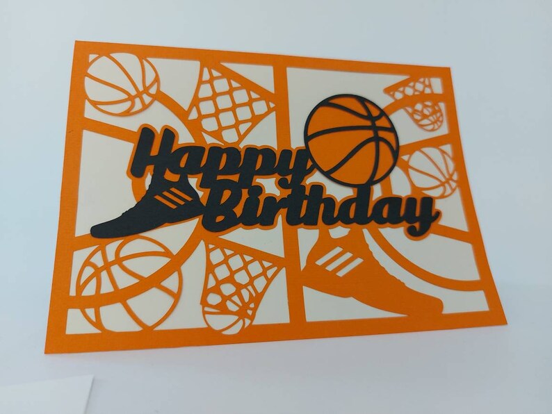 May include: Orange card with a black cut-out design of a basketball, a shoe, and a net. The card says "Happy Birthday" in black.