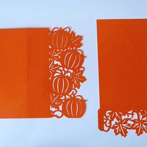 May include: Orange card with a pumpkin and leaf design cut out. The card is folded in half and the cut out design is on the right side of the card.