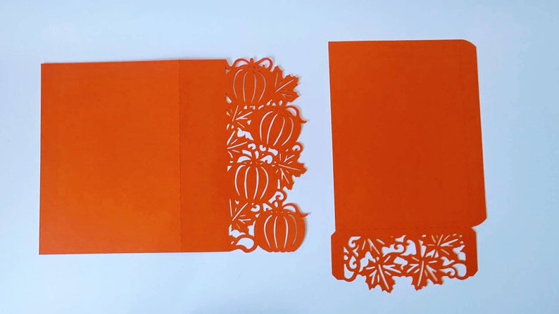 May include: Orange card with a pumpkin and leaf design cut out. The card is folded in half and the cut out design is on the right side of the card.