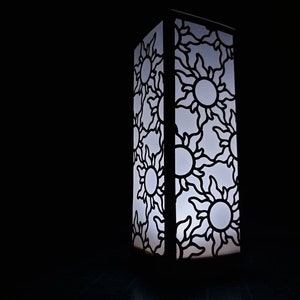 May include: A white lamp with a black cutout design of suns. The lamp is lit and casting a warm glow.