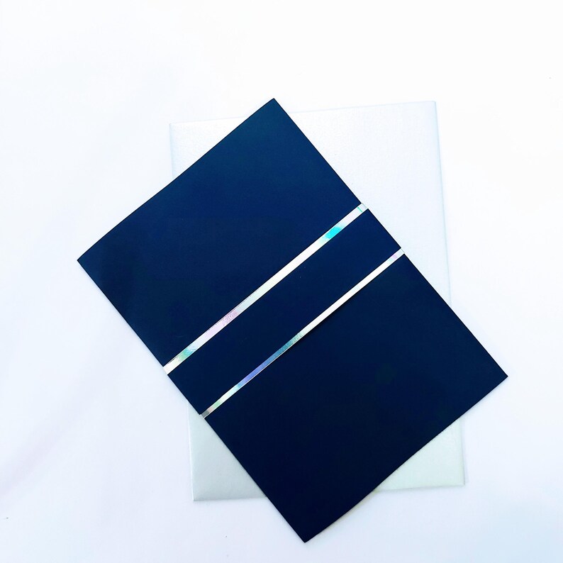 May include: A dark blue card with two silver holographic stripes. The card is folded in half and is sitting on top of a white card.
