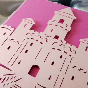 May include: A pink card with a white paper castle cut out. The castle has multiple towers and windows.