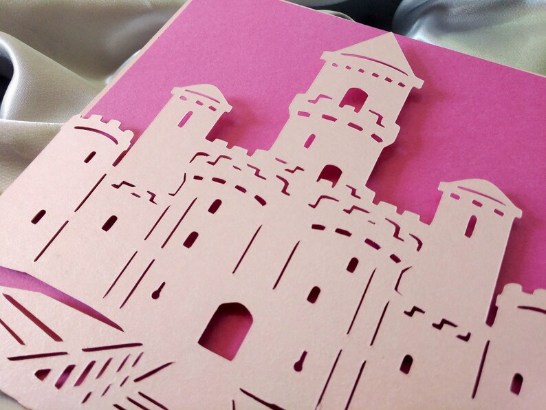 May include: A pink card with a white paper castle cut out. The castle has multiple towers and windows.