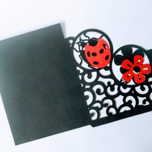 May include: Black card with a cut-out design of a ladybug and flower. The ladybug is red with black spots and the flower is red with a black center.