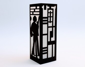 May include: A black silhouette of a person standing in a geometric patterned lamp. The lamp is made of black metal and has a white frosted glass panel.