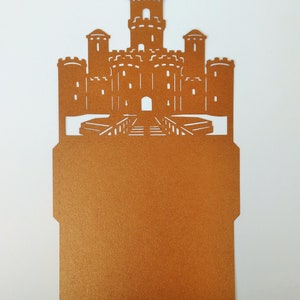 May include: A brown paper castle-shaped card with a cut-out design. The card is blank inside and can be used for invitations, announcements, or other special occasions.