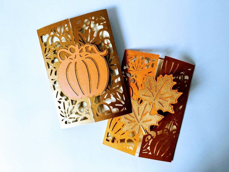 May include: Two folded cards with intricate cut-out designs. One card features a pumpkin with a gold background, while the other card has a brown background with leaves.