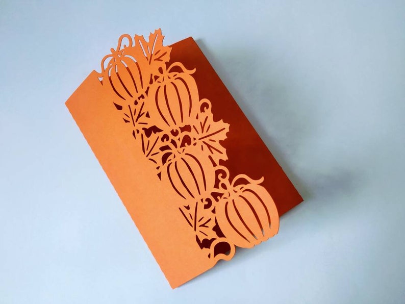 May include: Orange card with a decorative cut-out design of pumpkins and leaves. The card is folded in half.