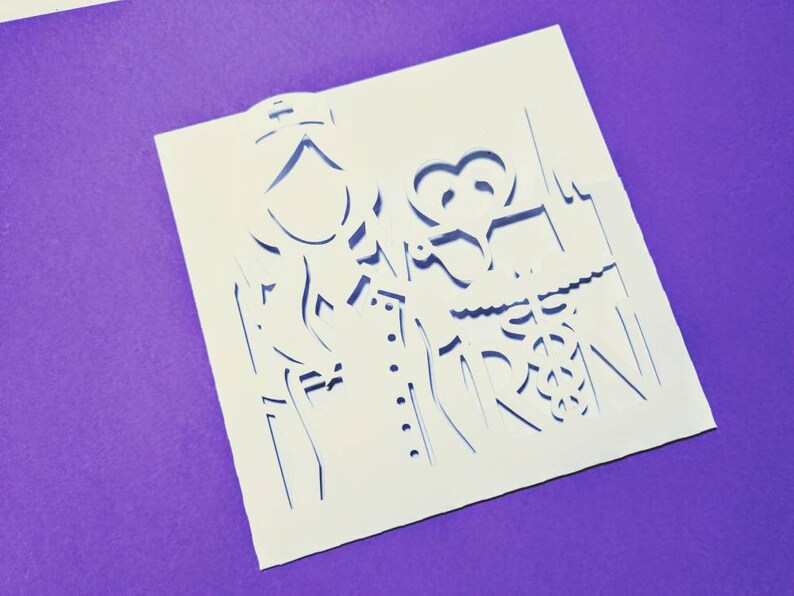 May include: White paper with a detailed cutout design of a couple holding hands. The design is intricate and includes a heart shape.