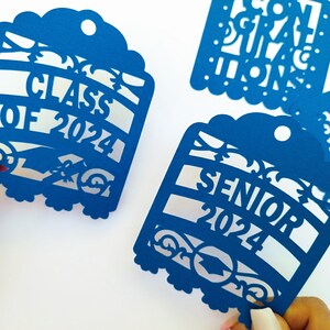 May include: Four blue paper cut-out graduation decorations. Each decoration features a different graduation-themed message: "Class of 2024", "Senior 2024", "Congratulations", and "You Did It!"