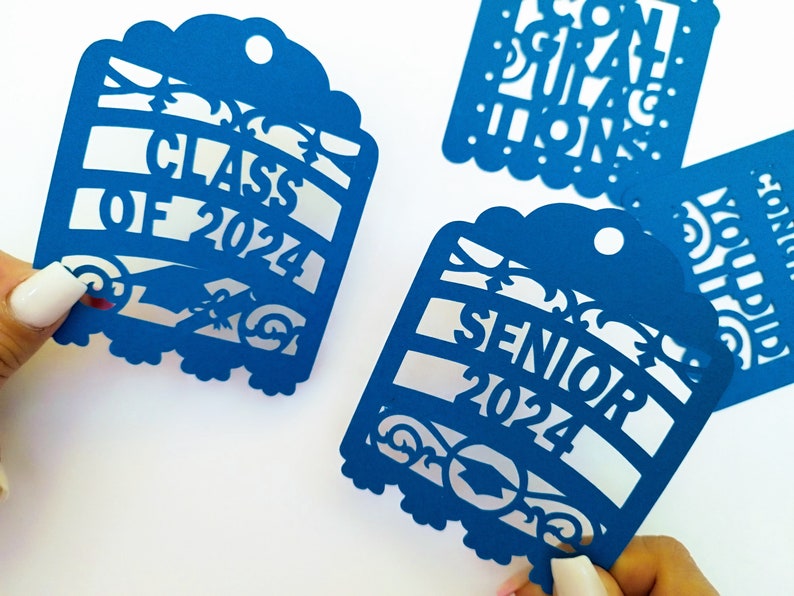 May include: Four blue paper cut-out graduation decorations. Each decoration features a different graduation-themed message: "Class of 2024", "Senior 2024", "Congratulations", and "You Did It!"