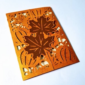 May include: A brown card with a cut-out design of fall leaves and pumpkins. The card is folded in half and has a textured surface.
