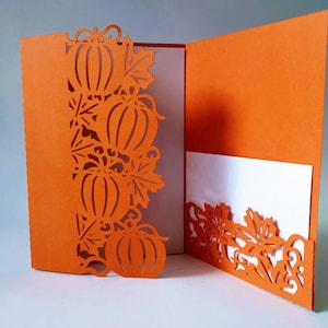 May include: Orange card with a cut-out design of pumpkins and leaves. The card is folded in half and has a white insert.