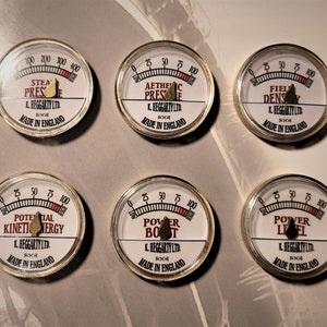 May include: Six round gauges with metallic rims and white faces. Each gauge has a needle and a scale from 0 to 100 or 400. The gauges display text such as "Steam Pressure" and "Power Level". The text "K. Heggarty Ltd. Made in England" is also visible.