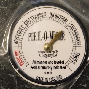 Peut inclure: Un indicateur circulaire blanc avec une aiguille noire et des marques noires. L'indicateur est intitulé "Peril-O-Meter" et comporte des marques pour "Apply Gin!", "Hot Tea Req'd", "Oh Bother!", "Shenanigans", "Yawn!!", et "Panic!!!". L'indicateur est fabriqué en Angleterre.