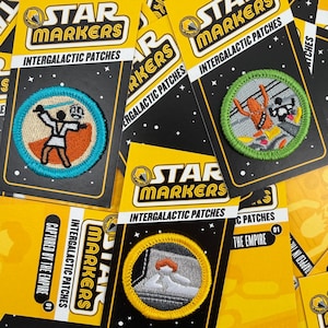May include: A collection of "Star Markers Intergalactic Patches" on yellow and black backing cards. The patches feature embroidered designs of characters and scenes. The cards have the text "Captured by the Empire" and "Training".