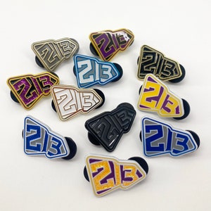 May include: A collection of 10 enamel pins featuring the number "213" in various colours and designs. The pins are shaped like a rocket ship and have a shiny finish.