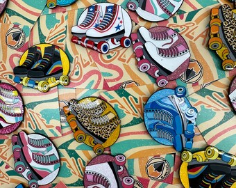 Könnte beinhalten: Eine Sammlung bunter Rollschuh-Emaille-Pins mit Glitzerakzenten. Die Pins zeigen verschiedene Designs, darunter Leopardenmuster, Sterne und Streifen. Die Pins werden auf einem Hintergrund aus bunten, wellenförmigen Mustern präsentiert.