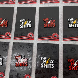 May include: A close-up of ten black and red cards with the text "The Holy Shits" printed on them. The cards are arranged in two rows of five. The cards are all the same size and shape.