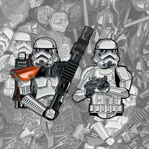 Può includere: Due spille smaltate con disegni di Stormtrooper. Una spilla raffigura uno Stormtrooper con una spallina arancione e una grande arma nera. L'altra spilla mostra uno Stormtrooper che tiene un blaster. Lo sfondo è un motivo in scala di grigi di vari personaggi di Star Wars.