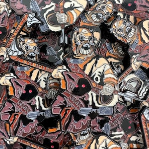 May include: A collection of enamel pins featuring characters from Star Wars. The pins are in various colors, including black, white, brown, and red. The pins are all different sizes and shapes, and they are all very detailed.