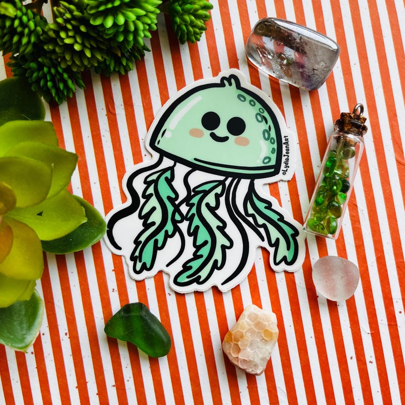 May include: A green and white cartoon jellyfish sticker with a smiling face. The sticker is on a striped orange and white background with other small objects.
